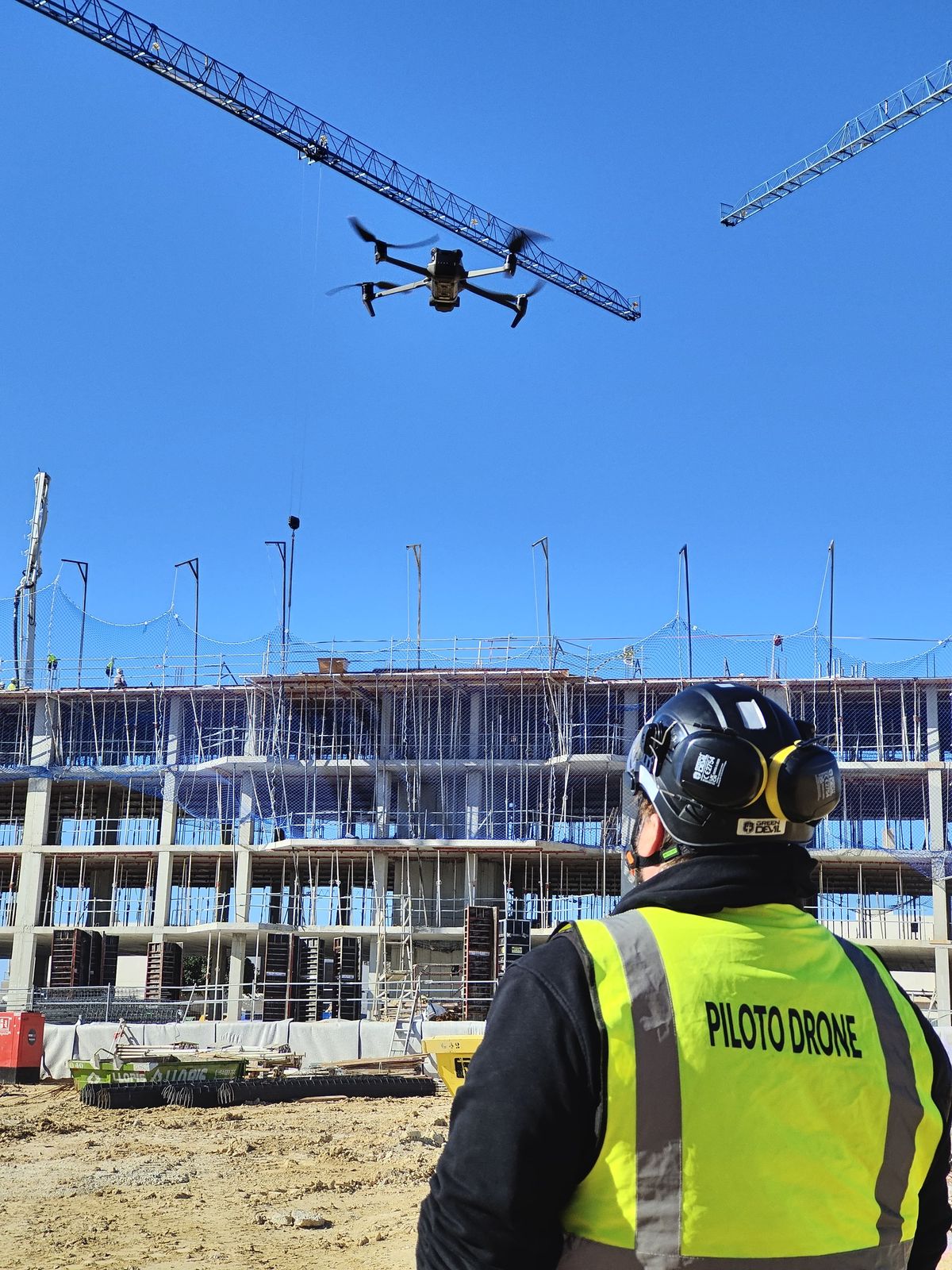 Piloto de dron operando junto a una grúa de obra